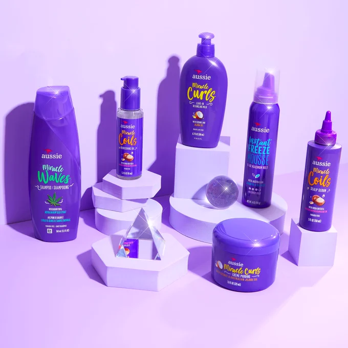 Collection of Aussie haircare products on purple background and shapes