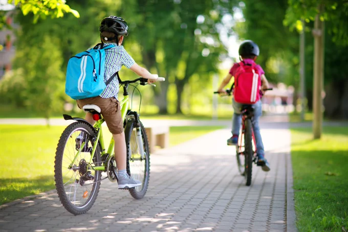 Two children wearing backpacks and helmets riding on bikes. 