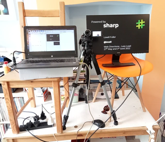 Laptop, monitor and camera precariously balanced on chairs and a table.