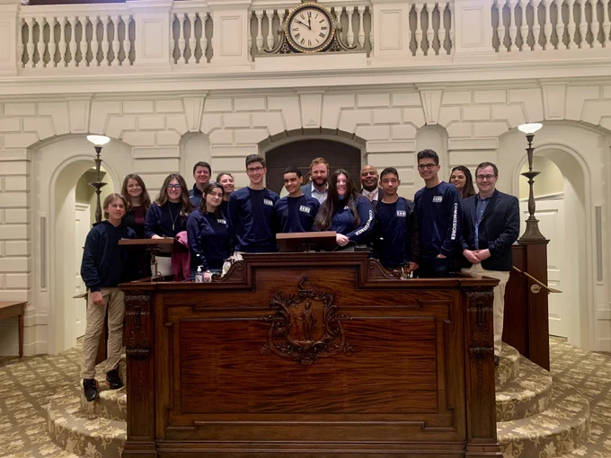 Barnstable Youth Commission students pose for a picture at the podium in the Senate Chambers with Senator Cyr, Rep Diggs, and Rep Scanlon.