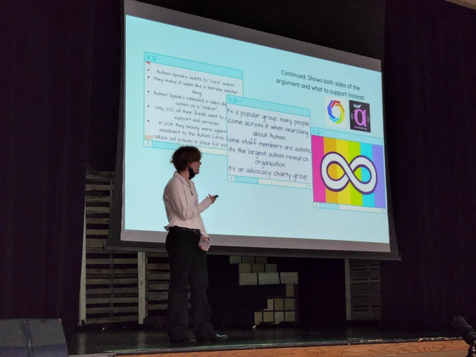A student on stage, next to a slideshow screen with text and graphics about disability rights and the autism community.