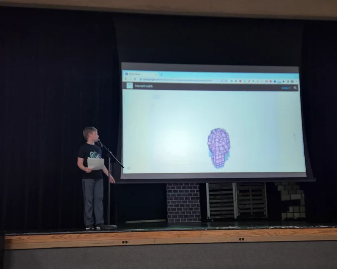A student on stage, next to a website screen with text about mental health and a 3D model of the human brain.