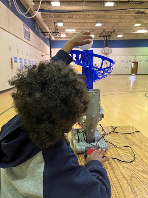 picture taken from the back. student reaching to place baseball in top of pitching machine.