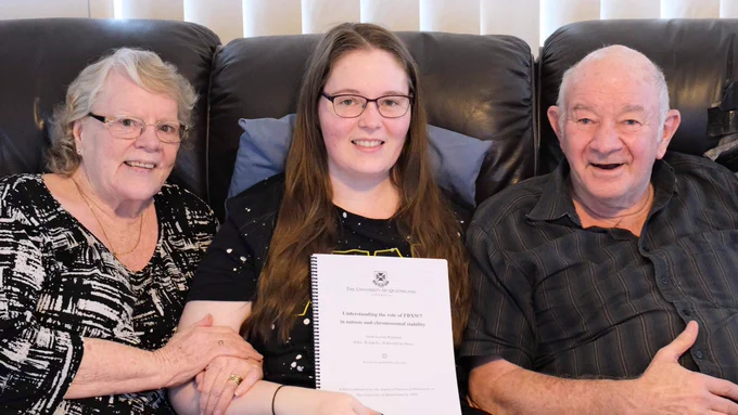 Me sitting with my two parents on a couch; my mum is on my left and my dad is on my right. I’m holding a spiral-bound printed copy of my PhD thesis.