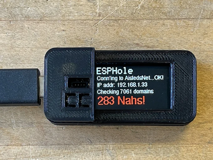 An Adafruit ESPHole: an open-source hardware gadget the size of a matchbox with a small screen that reads 'ESPHole/Conn'ing to Aisleds.Net...OK!/IP addr: 192.168.1.33/Checking 7061 domains/283 Nahs!