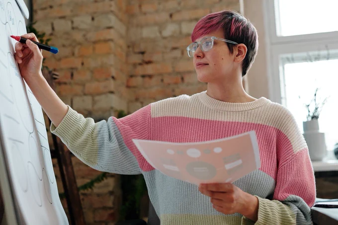 young person in a colourful jumper writing on a flipchart