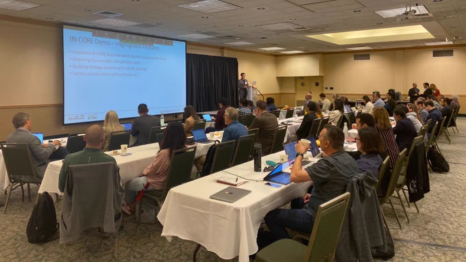 Jong Lee gives a talk at Colorado State University in a large conference room full of people. The screen highlights improved IN-CORE documentation, how to acquire Census data with pyincoe-data, building damage analysis, and visualizations with pyincore-viz.