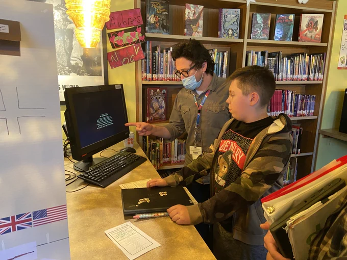 a teacher and a student look at a video on a monitor. 