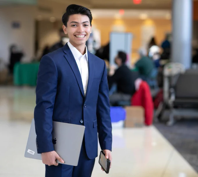 A portrait of Concha-Lopez in a navy suit, holding a laptop.