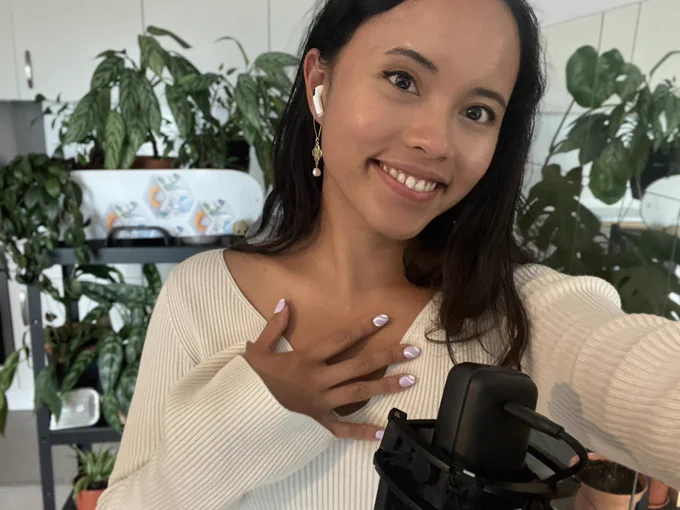 A selfie of me with my hosting set up: a mic, plant shelves, Gitpod skateboard and of course, purple spirally nails.