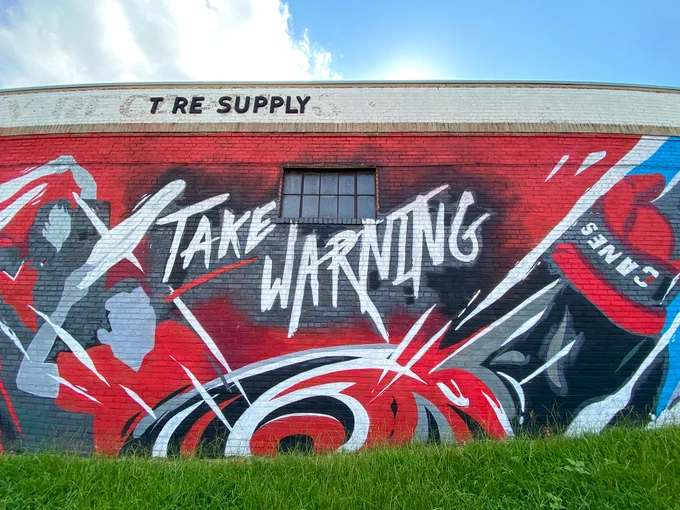 A mural on a brick wall depicting hockey fans waving towels above their heads. Text reads "take warning" 