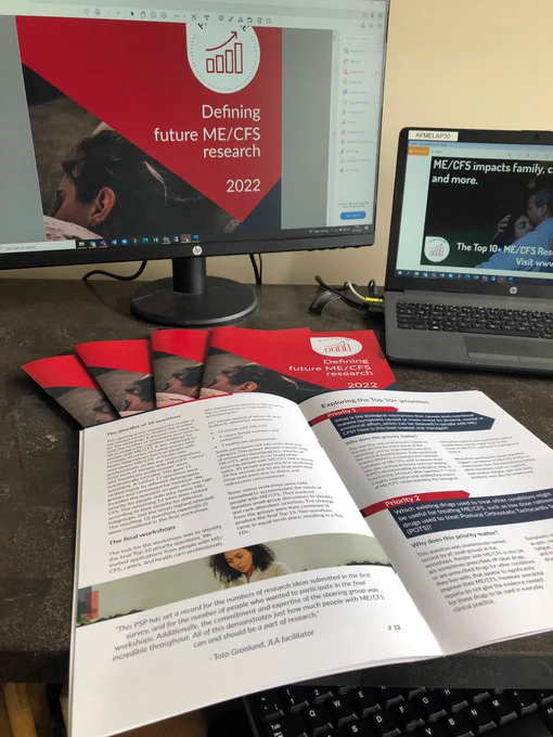 A computer and laptop screen show have the Defining Future ME/CFS Research report showing, while paper copies lay in a fan on the table in front. 
