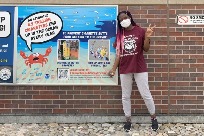 A student posing next to a cigarette debris prevention poster.