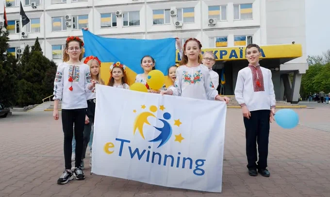 Ukrainische Schülerinnen und Schüler vor einem Schulgebäude, die eine eTwinning-Flagge hochhalten