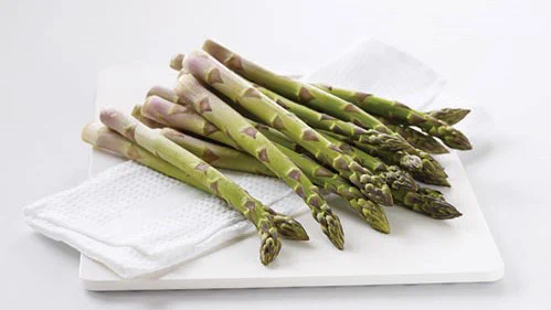 A pile of asparagus on a white cutting board