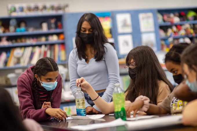 Weyanoke ES students carefully add materials to their water bottles, creating the lava lamp, as a TJHSST student stands and watches.