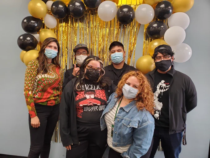photo of graduating library students and their supervisors. they are wearing masks and in front of a gold curtain and black, gold, and white balloons.