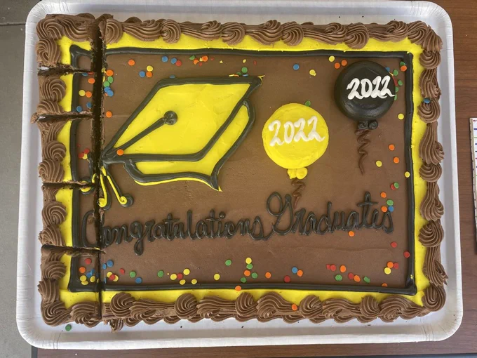 a chocolate cake decorated with black and yellow frosting that says "congratuations graduates 2022"