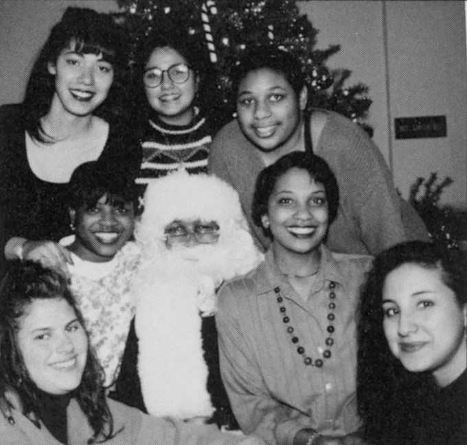 A group of Black and white women pose with Santa Claus in front of a Christmas tree. 