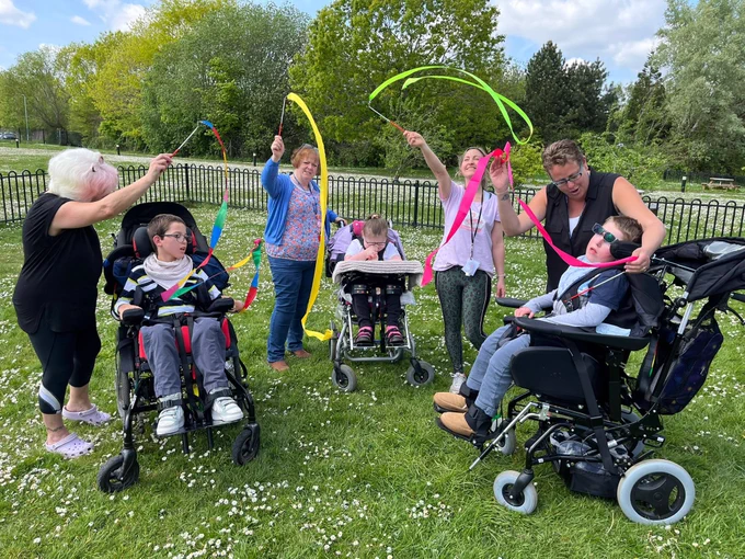 Image description: a photo of 3 young people in wheelchairs and 4 adults waving colorful ribbon wands.
