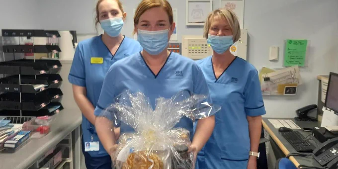 Three midwives, standing in an office. The midwife in the centre is holding a wrapped bag of treats.