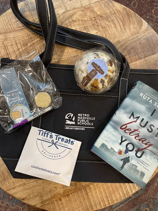 A tote bag with an autographed book by Ruta Sepetys and dessert items.
