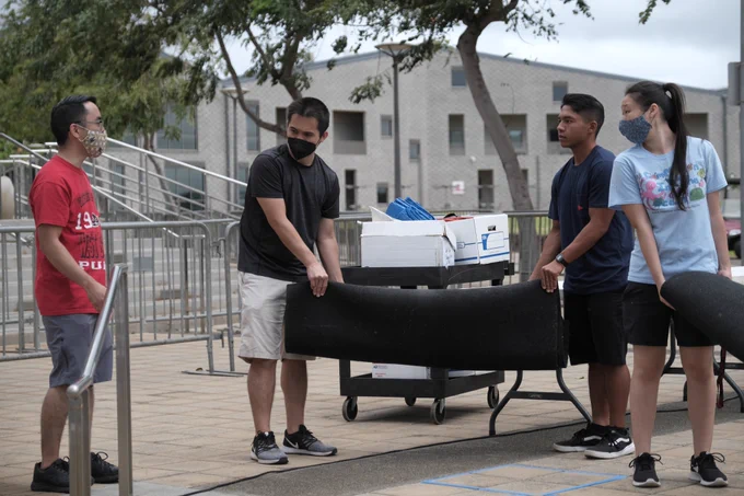 Four people setting up black mats outdoors.