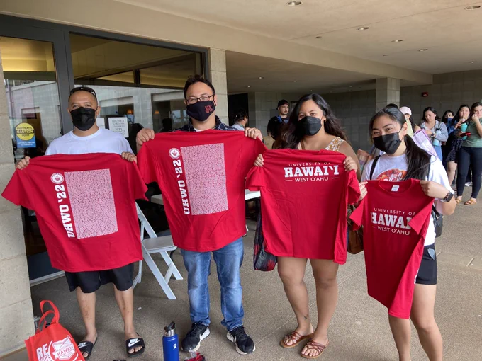 Four people wearing black face masks and holding up red T-shirts.