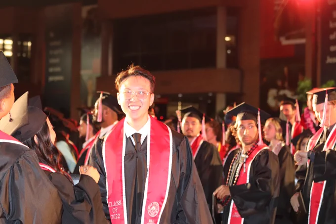 Graduate standing and smiling amongst other graduates.