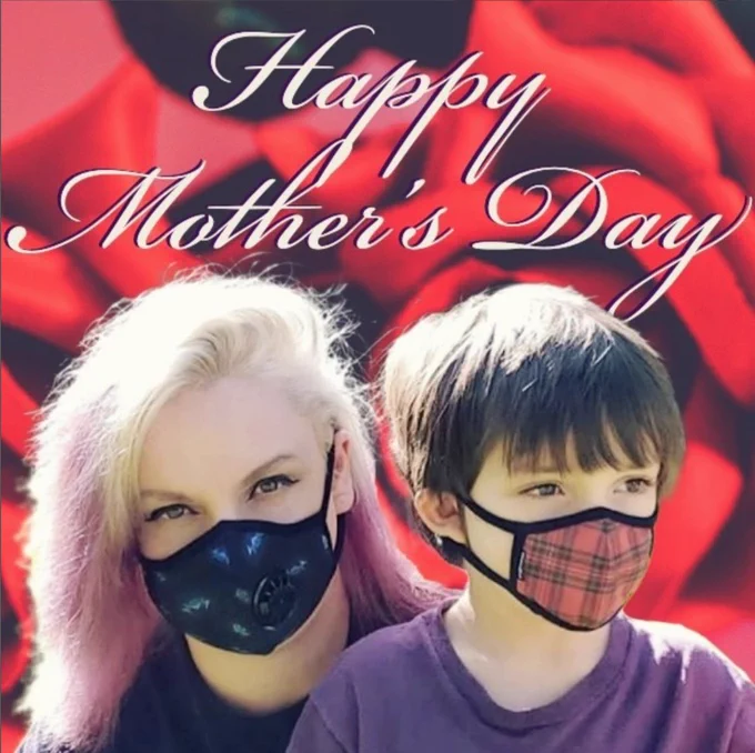 A blonde mother with purple highlights in her hair and a black mask sits with her young son who has dark hair and a red plaid mask. Behind them is a digital background of red roses. Above them in white, cursive text reads, "Happy Mother's Day."