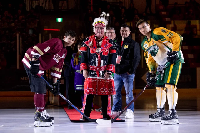 Membertou Chief Terrence Paul drops a hockey puck for two uniformed players on an ice surface