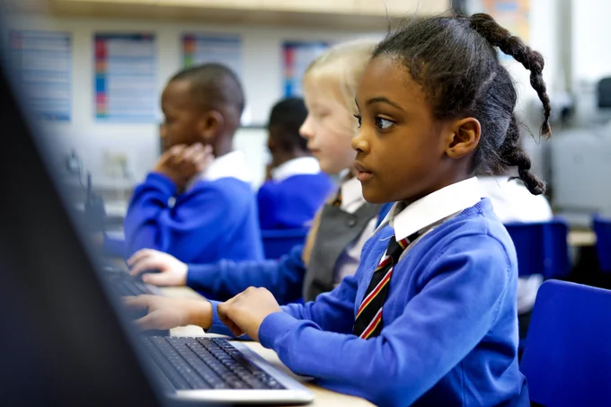 Young pupils at a school sitting at and engaging with a computer.