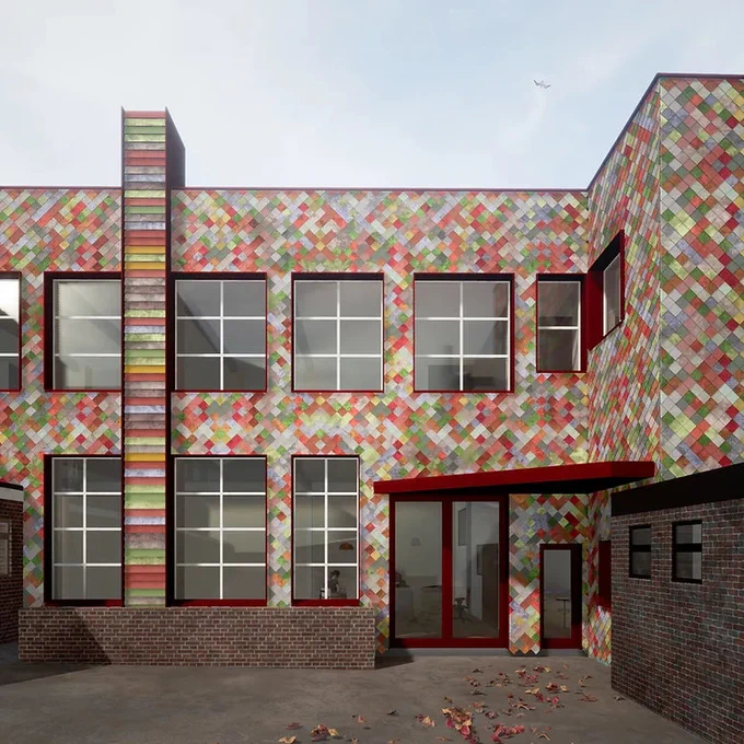 Image of a two storey former industrial building.  It is covered in bright multicoloured tiles. There are autumn leaves scattered on the ground in the yard in front.