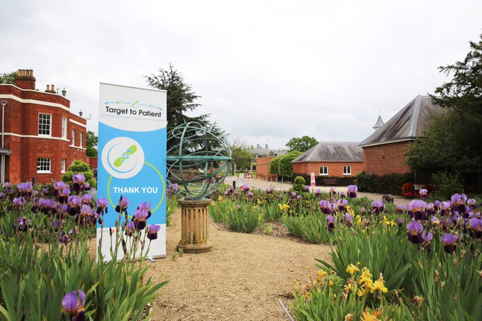 A banner saying thank you stands in the grounds of the Hinxton Hall garden surrounded by purple irises.