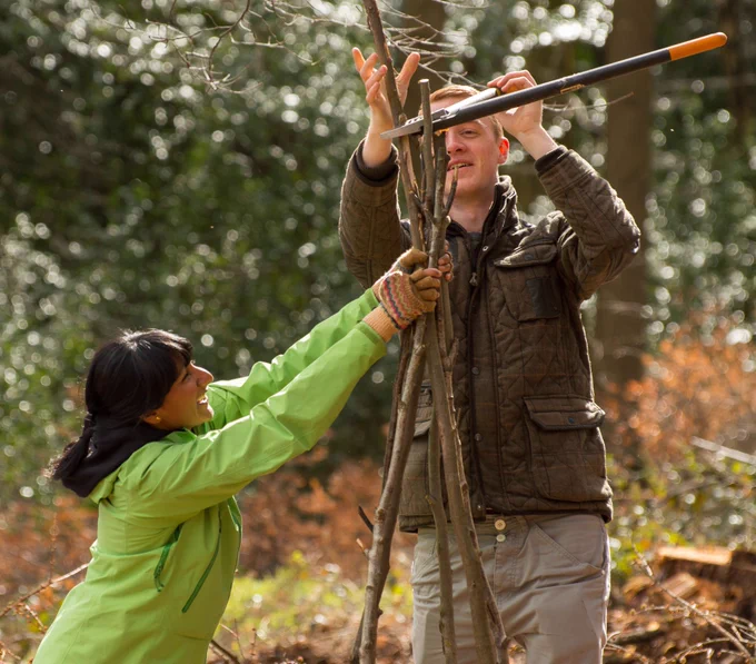 Two people creating a structure from branches in the woods.