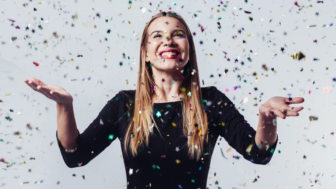 Confetti falling down over a young woman. She's smiling with hands reached out.