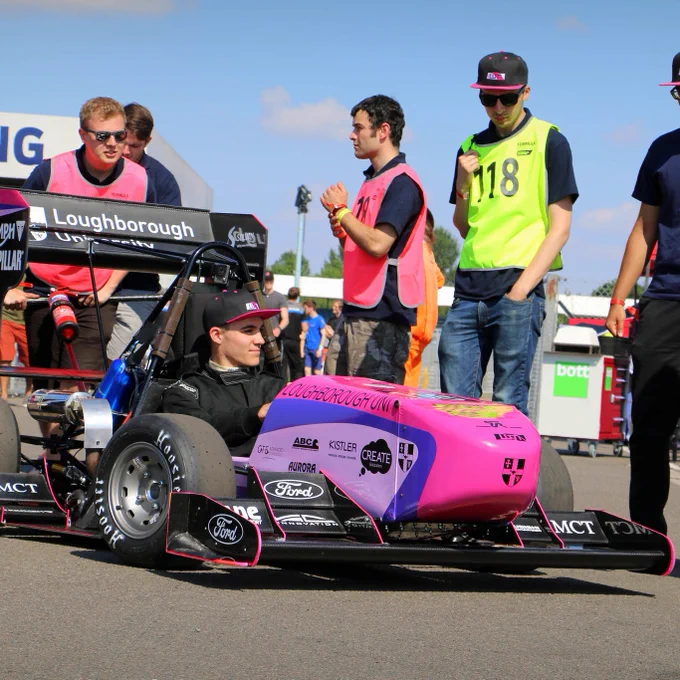 The team from University of Loughborough push their driver and his bright pink car and across the paddock at Silverstone in the sun