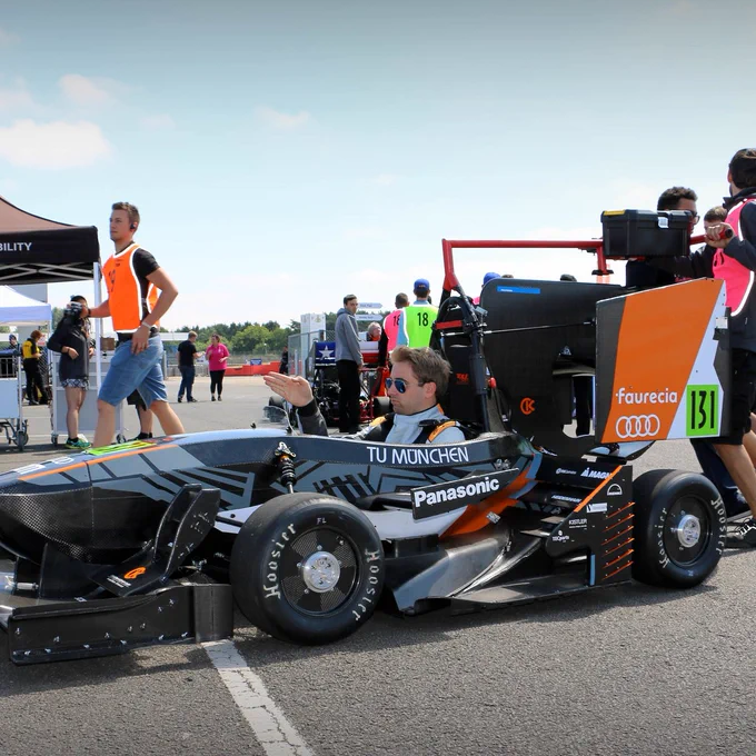 The TU Muenchen car and its driver stops for a moment in the Silverstone paddock while the team member pushing behind shouts at another colleague