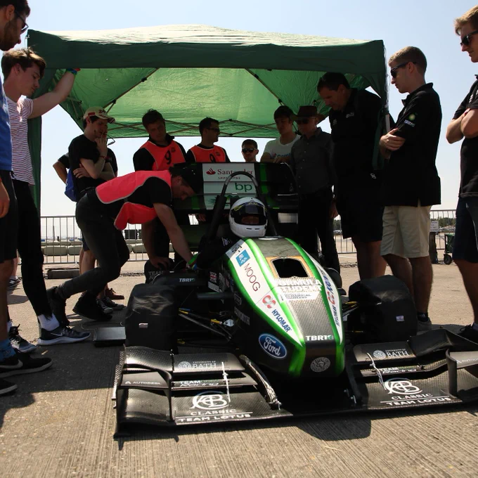 The University of Bath team crowd round their car under a portable gazebo turned parasol to get out of the sun.
