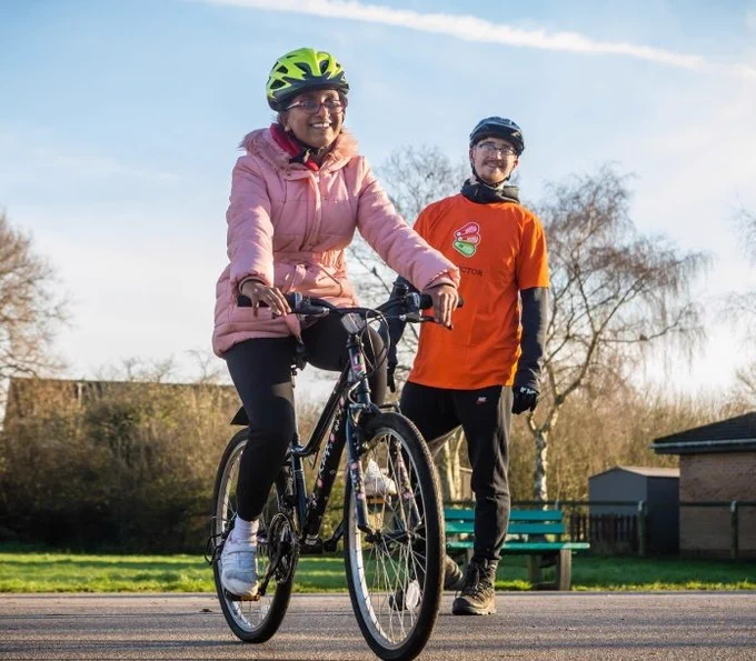 Photo of a lady riding a bike with an instructor looking on