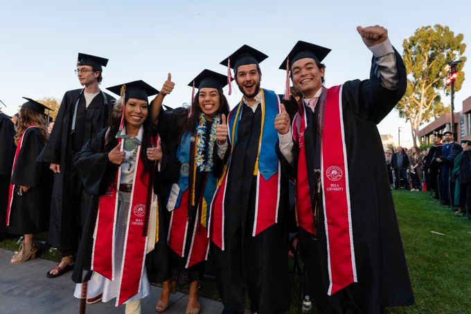 Graduates posing with thumbs up in group photo.