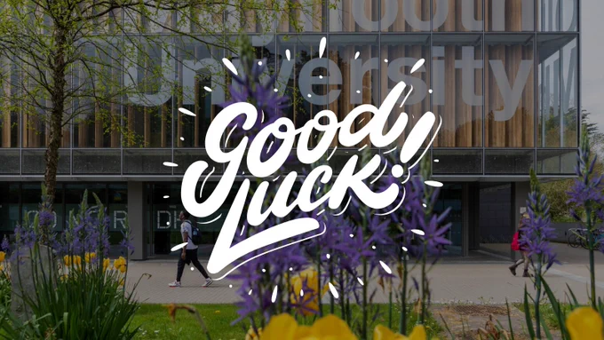 Text reads "Good Luck!", background image is of spring flowers on campus with the front of the library in the background, the view from the sloped entrance to campus from the Kilcock road