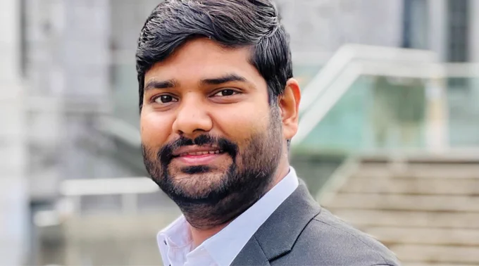 A closeup of Lucky Garg. He looks into the camera directly. He has a beard and wears a collared shirt and blazer.