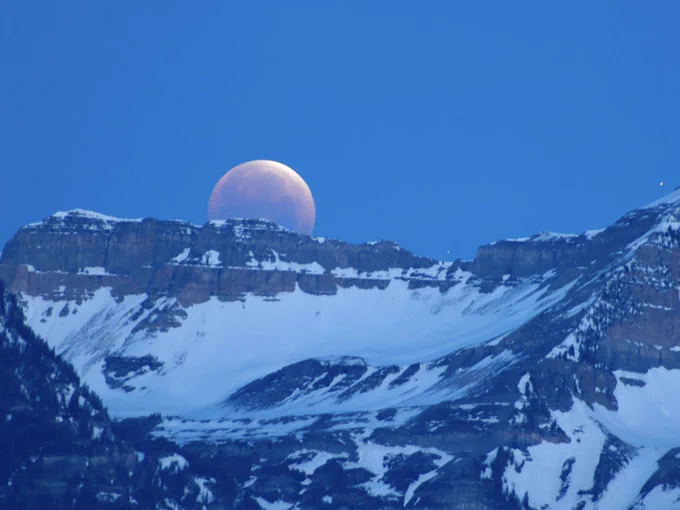 The partially eclipsed Moon sets behind a rocky mountain range