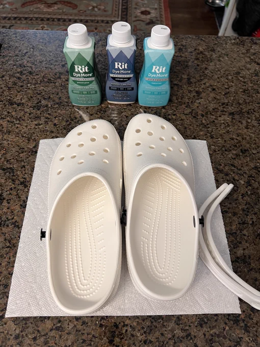A photo of a pair of white crocs with 3 bottles of dye