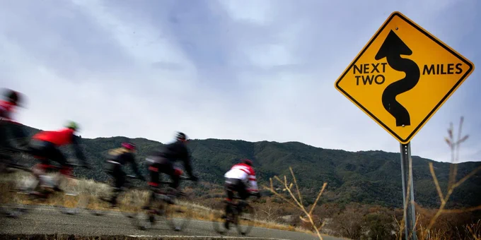 5 cyclists on mountain road. Sign showing wavy route for next 2 miles