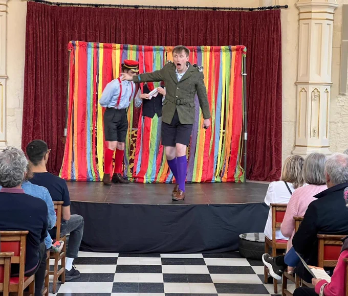 Actors in period dress perform on a small, brightly colour stage set up in a Church