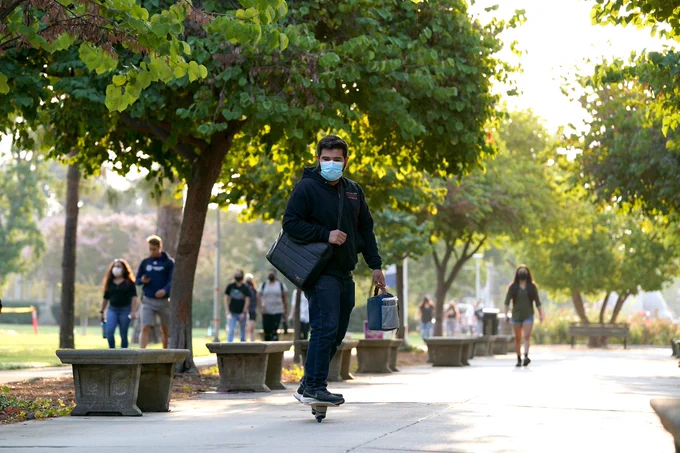 Masked student skateboarding across the Fresno State campus.