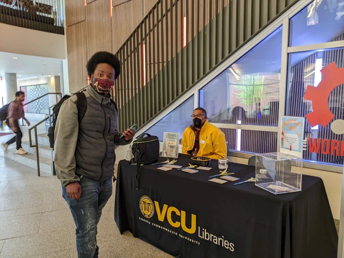 Student stands near a table with a postcard in hand