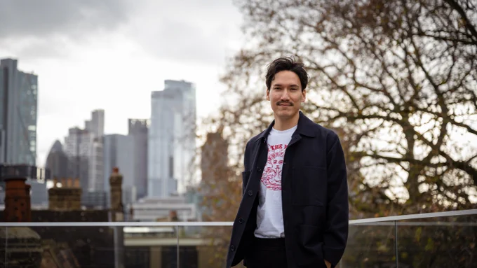 Brian Grellmann standing in front of the London skyline with a tree behind him.